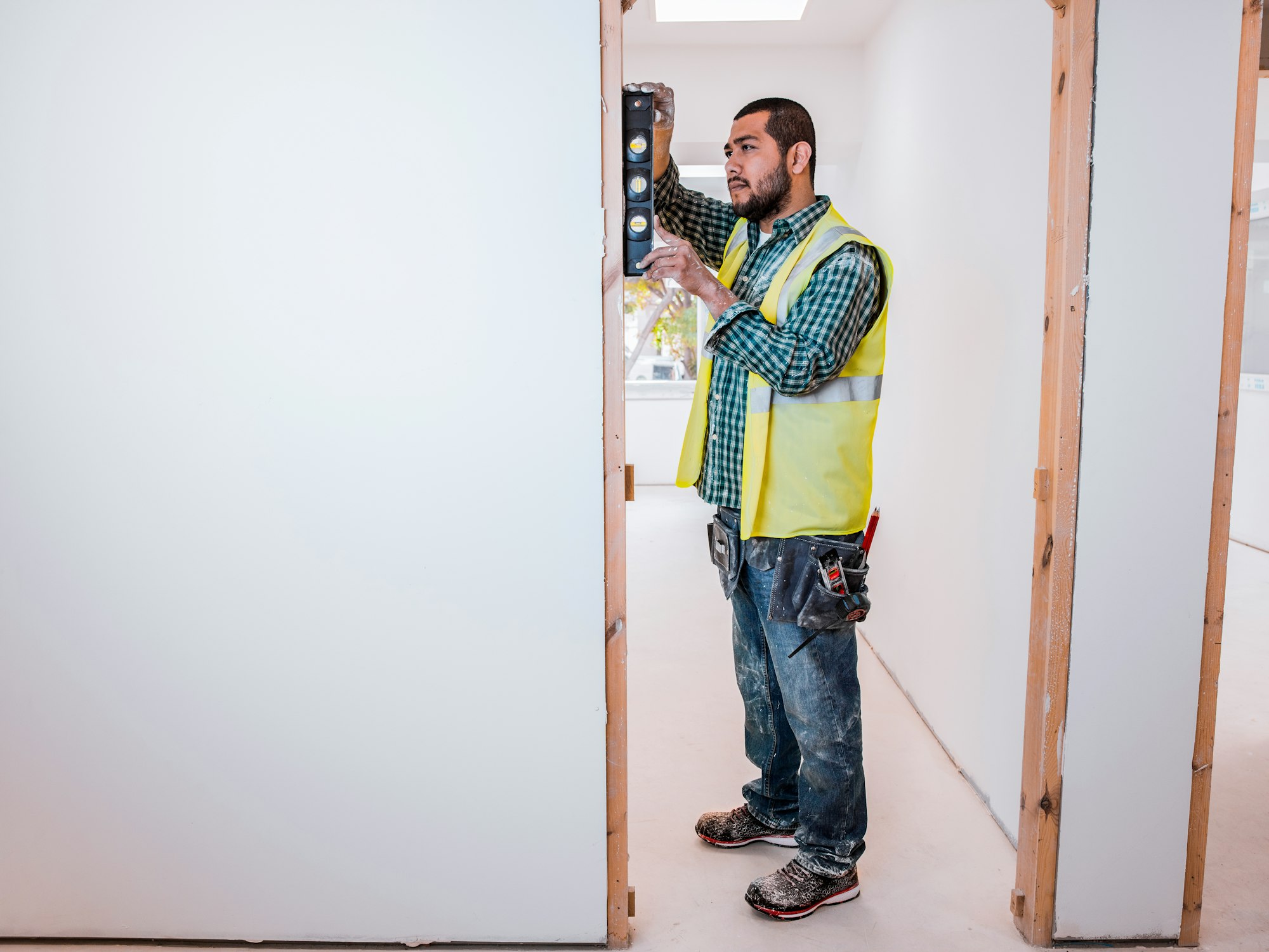 A Latin carpenter places a level on a door frame in a house under construction.