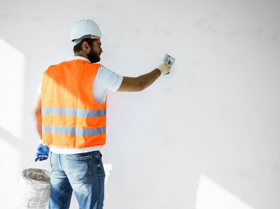 Plasterer in workwear smoothing wall surface of building indoors