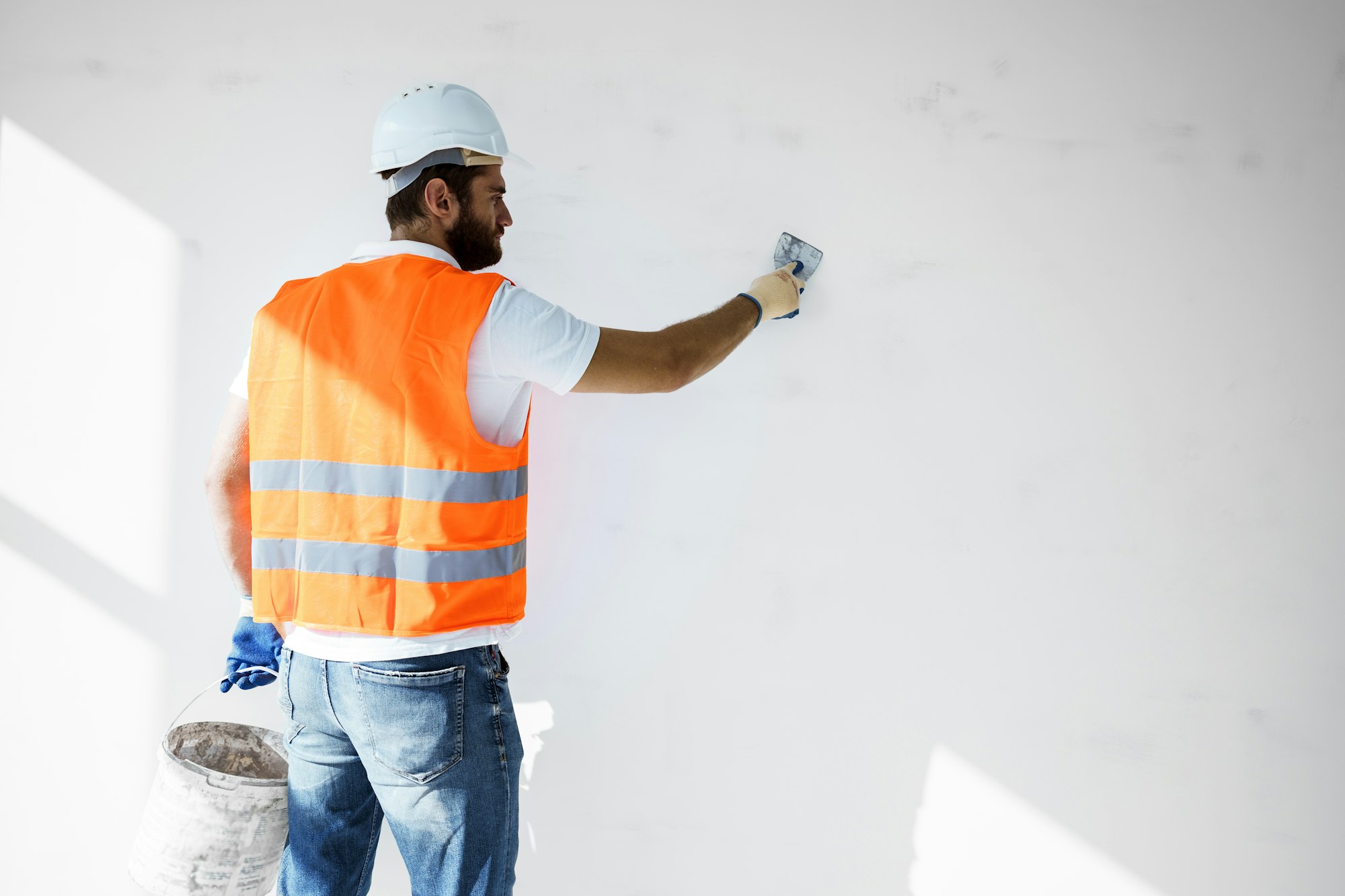 Plasterer in workwear smoothing wall surface of building indoors