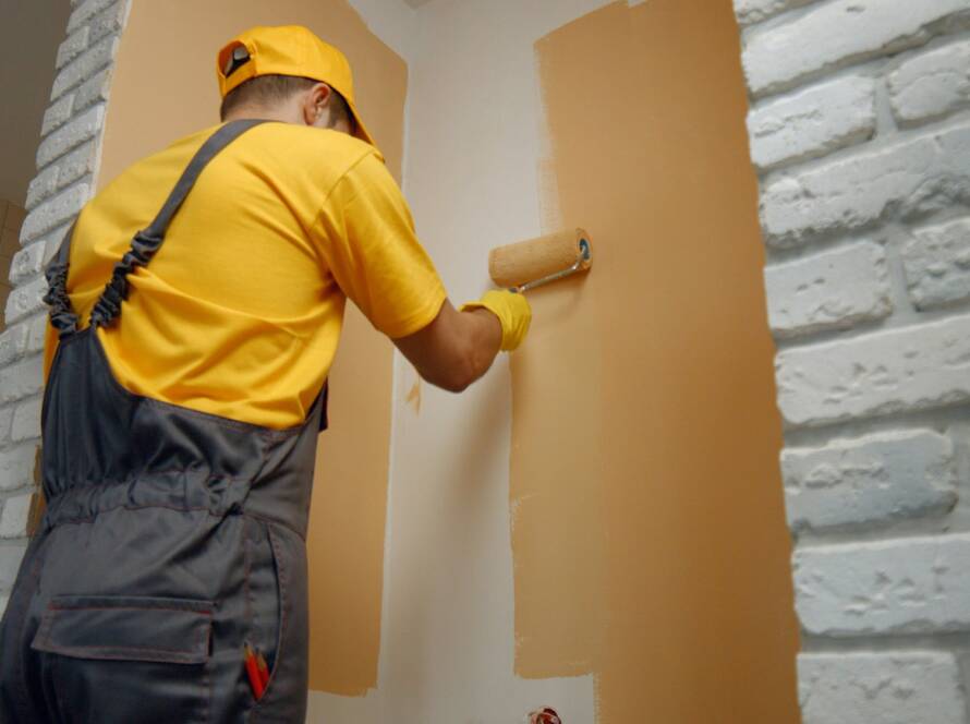Worker painting wall with paint roller.